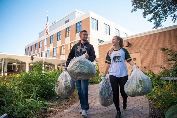 two students walking with garbage bags
